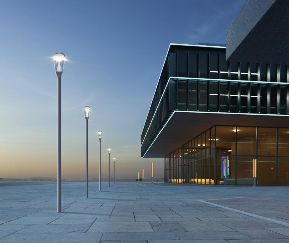 Illuminated post-top poles beside a contemporary plaza building at dusk